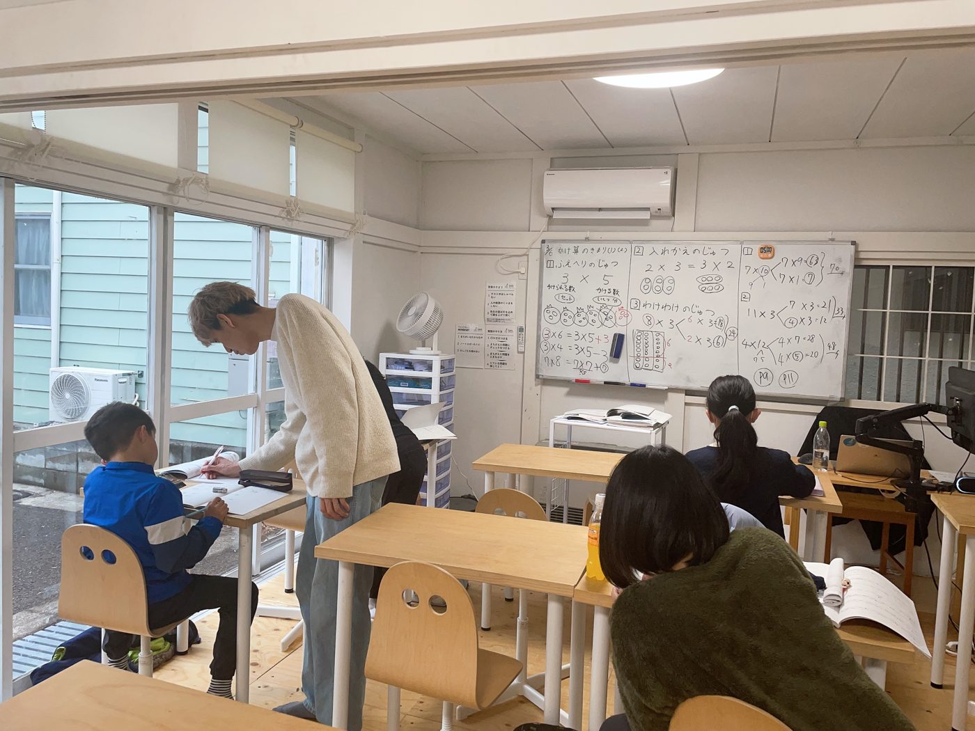 先生が席の横にかがんで、小学生の手元を一緒に見ている