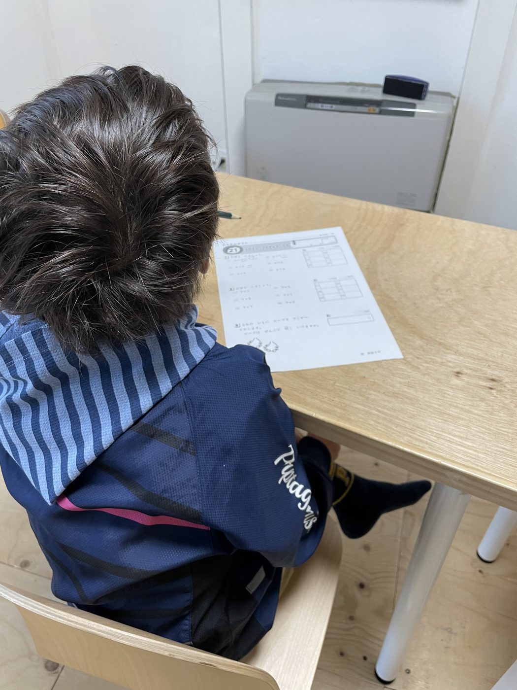 机に向かい、テスト用紙に自分で書き込んでいる小学生の後ろ姿